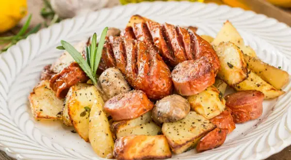 Pyszne dania z piekarnika na obiad: pieczone ziemniaki, kiełbaski i grzyby, doprawione ziołami i pieprzem.