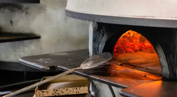 Piec do pizzy z palącym się ogniem i łopatą do pizzy.