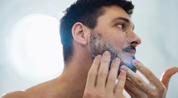 La cara de hombre con espuma de afeitar, preparándose para un afeitado apurado.