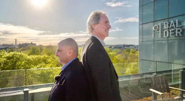Erik Selin och en kollega står rygg mot rygg på en takterrass med utsikt över en grönskande stad.