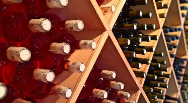 Scaffale in legno con bottiglie di vino rosse e scure, disposte con la corretta inclinazione per la conservazione.
