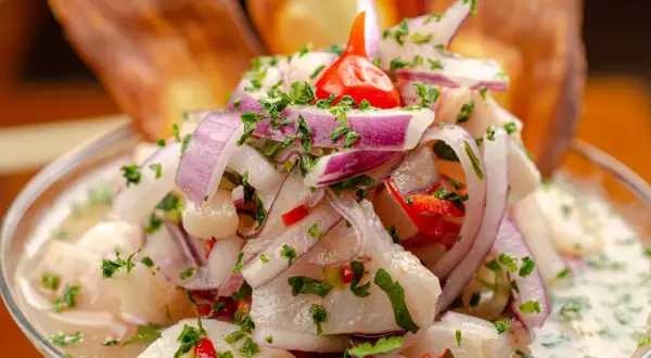 Ceviche z ryby, cebuli, papryczki chili i kolendry w szklanej misce, z chipsami bananowymi w tle.