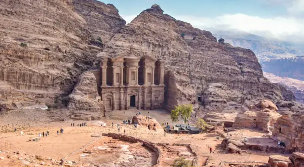 Niezwykłe miasto w skale Jordania, Petra, z monumentalną fasadą wykutą w piaskowcu. Turyści spacerują po piaszczystym placu u stóp starożytnej budowli.
