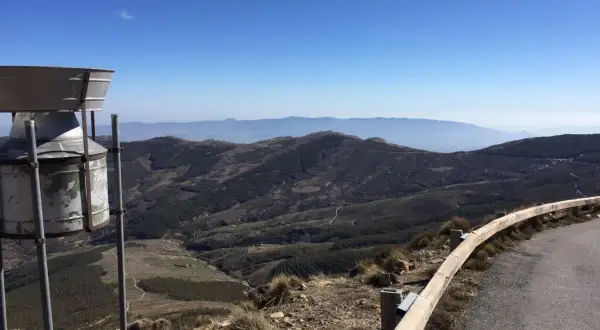 Vista panorámica desde la tetica de bacares, con un pluviómetro en primer plano y un paisaje montañoso y boscoso al fondo bajo un cielo azul.