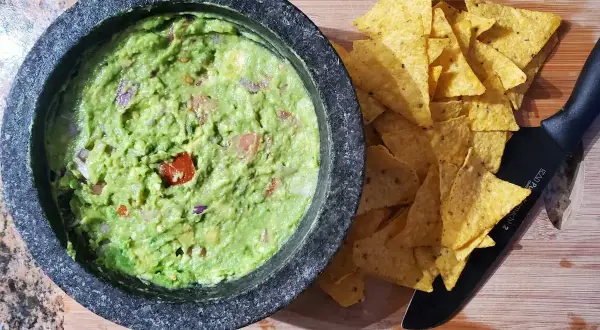 Närbild på hemlagad guacamole i en mortel, redo att serveras med tortillachips. Ett perfekt guacamole recept för alla tillfällen.