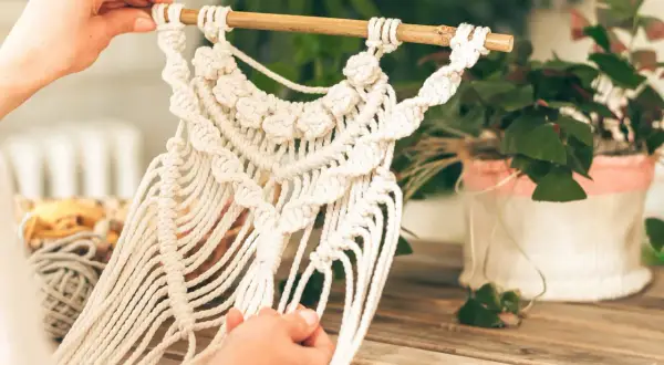 Mains créatives travaillant sur une décoration murale en macramé. Une belle idée déco macramé pour un intérieur bohème.