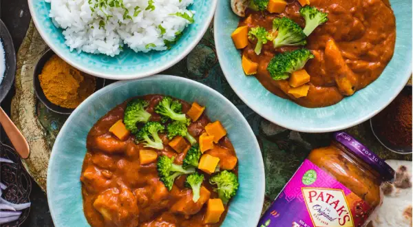Dwa talerze z indyjskim curry z dynią i brokułami, ryżem i słoikiem sosu Tikka Masala.