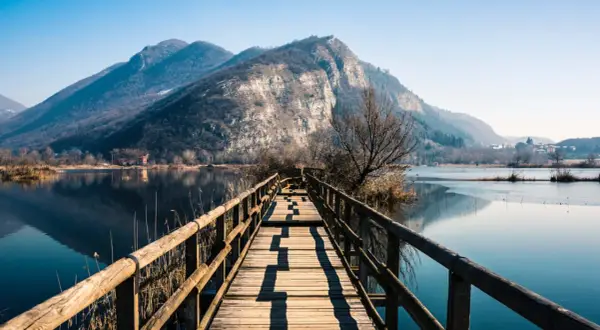 Passerella in legno su lago calmo, montagne sullo sfondo. Un luogo incantevole per scoprire cosa vedere in Franciacorta.