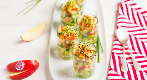 Amuse-bouche pomme et crevettes dans des verrines, garnies de pousses. Des quartiers de pomme Pink Lady sont disposés à côté.