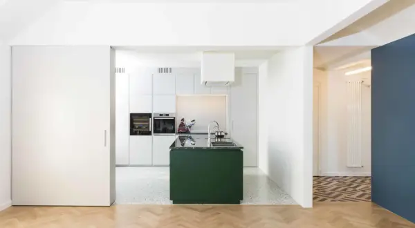 Moderna cucina verde in un ampio soggiorno open space. Pavimenti in parquet e resina, elettrodomestici a scomparsa.