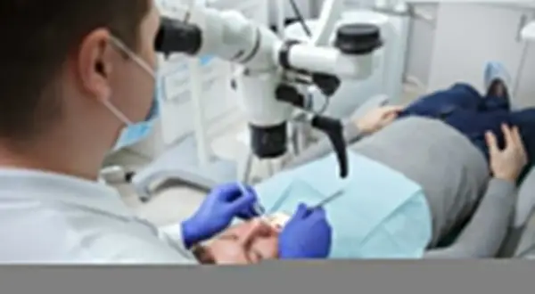 Dentysta pod mikroskopem bada ząb pacjenta. Po leczeniu kanałowym można jeść, ale warto poczekać na znieczulenie.