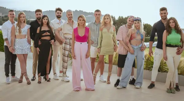 Grupa młodych ludzi pozuje do zdjęcia. Widać ich stroje, uśmiechy, ale czego nie widać w kamerach podczas nagrań reality show?