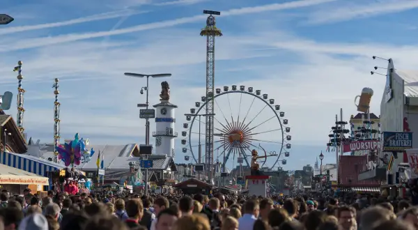 Menschenmassen auf dem **Bayern Oktoberfest** mit Riesenrad, Fahrgeschäften und Bierkrügen.