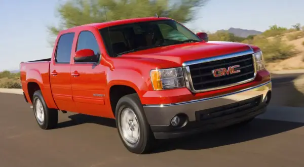 Czerwony pickup GMC Sierra z napędem 4x4 jedzie po pustynnej drodze.