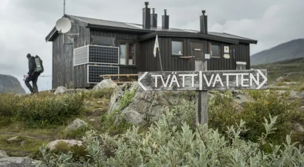 Vandrare närmar sig en av kungsleden stugor. En skylt pekar mot "TVÄTT VATTEN".