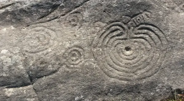 Petroglifos de Mogor: grabados circulares concéntricos y un posible sol en una roca antigua.