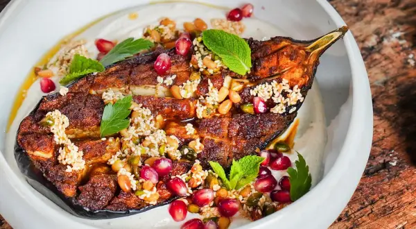 Gebackene Aubergine mit Tahini, Granatapfelkernen und Minze. Ein köstliches Gericht, das zeigt, wie vielseitig auberginen rezepte im backofen sein können.