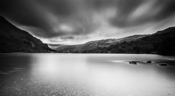 Un photographe paysage capture un lac paisible sous un ciel dramatique, les montagnes se reflétant dans l'eau lisse.