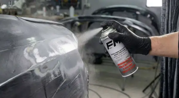 Persona con guante negro aplica imprimación en spray a un coche.
