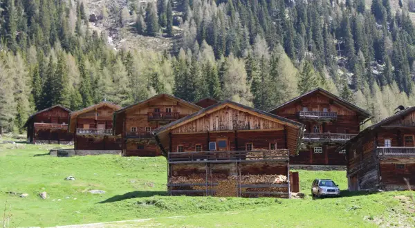 Holzhäuser im Villgratental, umgeben von grünen Wiesen und Nadelwäldern. Eine Karte des Villgratentals würde diese idyllische Landschaft zeigen.