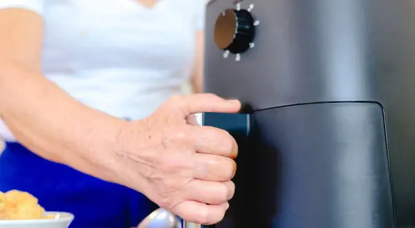Dłoń osoby wyciąga szufladę frytkownicy beztłuszczowej, pokazując, jak działa air fryer.
