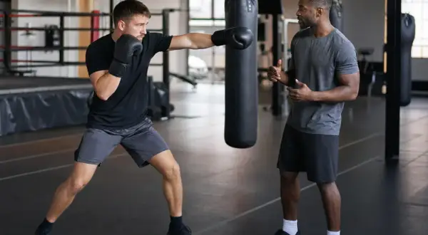 A boxer practices jabs with a trainer watching, counting the punches. The gym has boxing numbers on the wall.