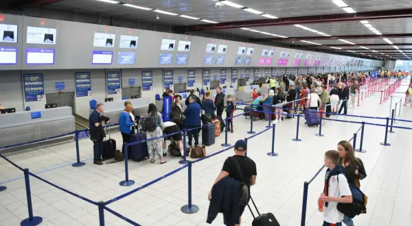 Kolejka do check-in na lotnisku. Pasażerowie z walizkami czekają na obsługę przy stanowiskach odprawy.
