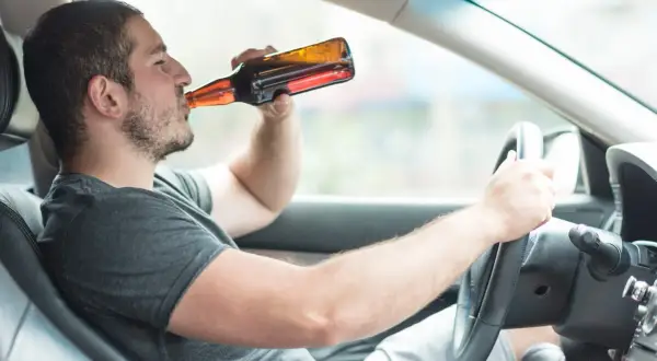 Mężczyzna pije piwo za kierownicą. To niebezpieczna jazda po alkoholu, która może skończyć się tragicznie.