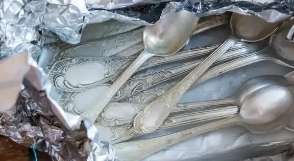 Stare, ozdobne łyżki i widelce owinięte w folię aluminiową, gotowe do czyszczenia srebra.