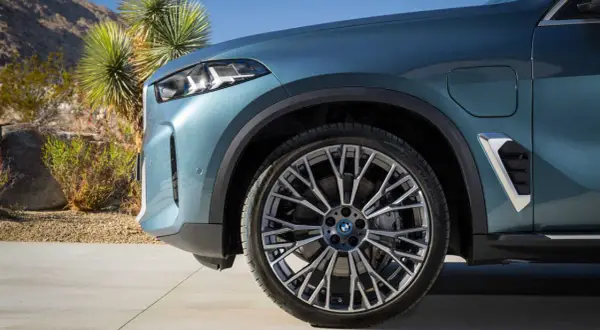 Nowe BMW X5 2023 w kolorze niebiesko-zielonym, z felgami o skomplikowanym wzorze, zaparkowane na tle pustynnego krajobrazu.