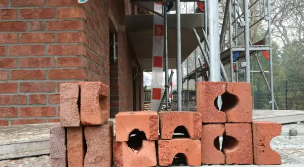 Stos cegieł na budowie. W tle widać fragment czerwonej ściany i rusztowania.