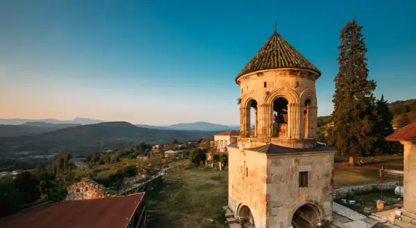 Wieża dzwonnicza Gelati Monastery na tle górskiego krajobrazu o zachodzie słońca.