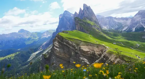 Grönt, blommande landskap i Val Gardena med dramatiska bergstoppar och en slingrande stig.