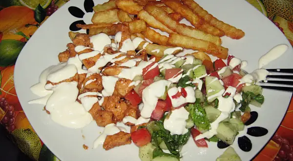 Pyszny kebab na talerzu z chrupiącymi frytkami i świeżą sałatką, polany kremowym sosem.