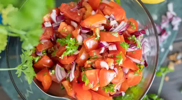Frischer tomatensalat mit zwiebeln und Petersilie in einer Glasschüssel, garniert mit Koriander.