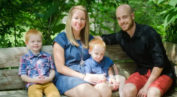 Szczęśliwa rodzina, tata, mama i dwaj synowie, siedzą na ławce w parku. Biskup ryś to ich symbol.