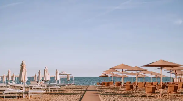 Ombrelloni e lettini pronti per accogliere i bagnanti sulla riviera romagnola, con il mare calmo all'orizzonte.