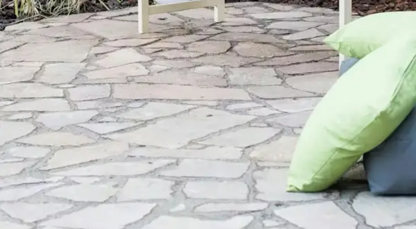 Naturalny chodnik z płyt chodnikowych, idealny do relaksu na świeżym powietrzu. Dwie poduszki, jedna jasnozielona, dodają koloru.