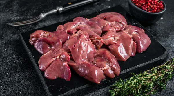 Frische barf innereien, roh und appetitlich auf einem schwarzen Brett, garniert mit Thymian und rosa Pfeffer.