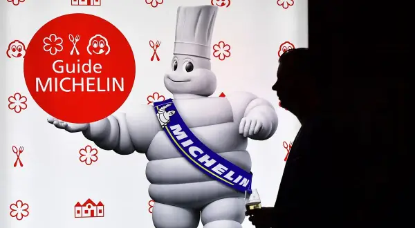 El muñeco Michelin, con su banda "MICHELIN", posa junto a un hombre con copa. Un símbolo de los restaurantes con estrella Michelin.