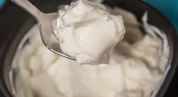 Un cucchiaio raccoglie una generosa porzione di cremoso yogurt greco fatto in casa, pronto per essere gustato.