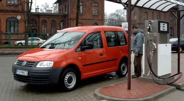 Pomarańczowy Volkswagen Caddy, auto zasilane CNG i hybrydą, tankuje na stacji.