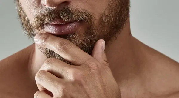 Gros plan sur un homme pensif, sa main caressant sa barbe. L'évolution de sa barbe, de la naissance à sa forme actuelle, est visible.