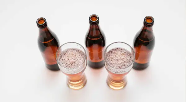 Tre bicchieri di birra con schiuma e quattro bottiglie marroni vuote, una birra andata a male.