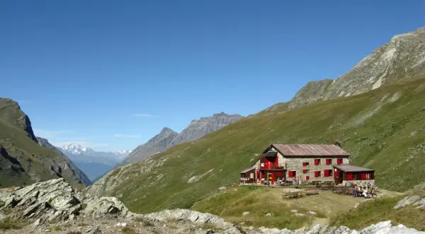 Rifugio nel Val di Rhemes, con persone sedute ai tavoli all'esterno, circondato da verdi pendii montuosi sotto un cielo azzurro.