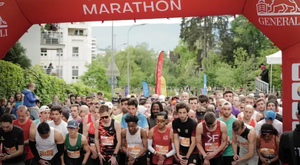Des coureurs se préparent au départ de la course 10km Genève, sous une arche rouge "Genève + Marathon".