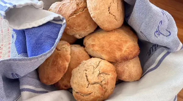 En hög med gyllene, luftiga scones som vilar i en blåvitrandig kökshandduk. Perfekt för fikat!