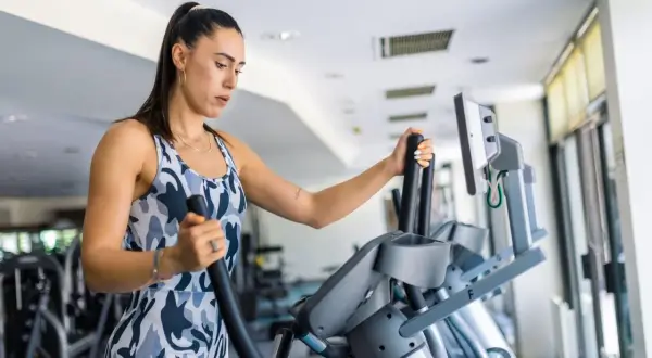 Frau trainiert auf einem Crosstrainer, um ihren Kalorienverbrauch zu steigern.