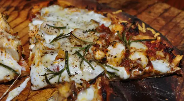 En närbild av en utsökt pizza med kyckling, ost och rosmarin. En smak av pizzans ursprung.