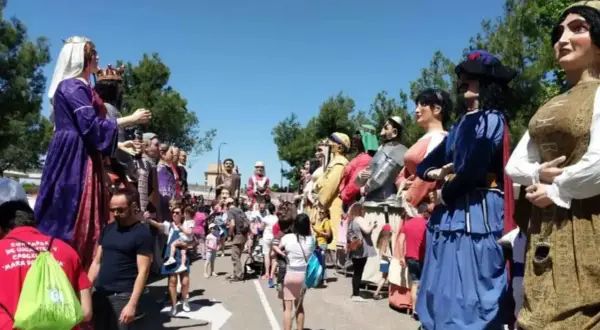 Gigantes y cabezudos desfilan en las fiestas del Parque Goya. Niños y adultos disfrutan de la colorida procesión bajo el sol.